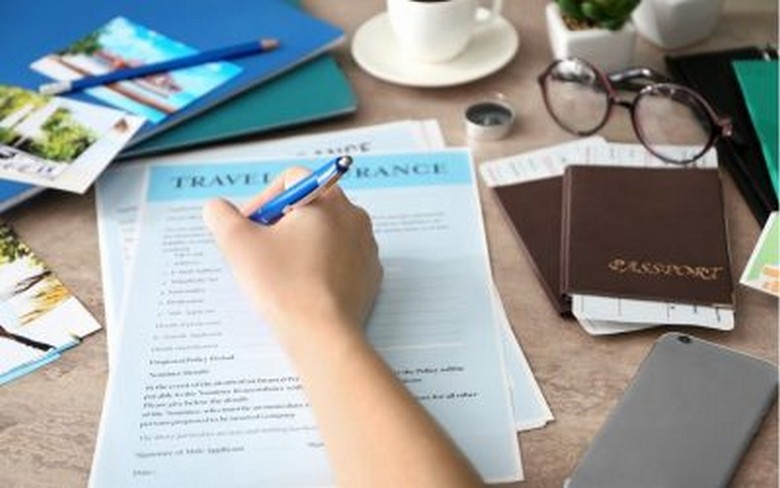 Du khách cầm hồ sơ bảo hiểm du lịch và hộ chiếu trước chuyến đi