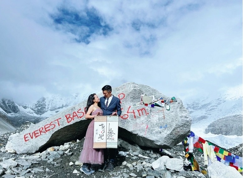 Du khách chụp ảnh trước tấm bia Everest Base Camp với đỉnh Everest phía sau